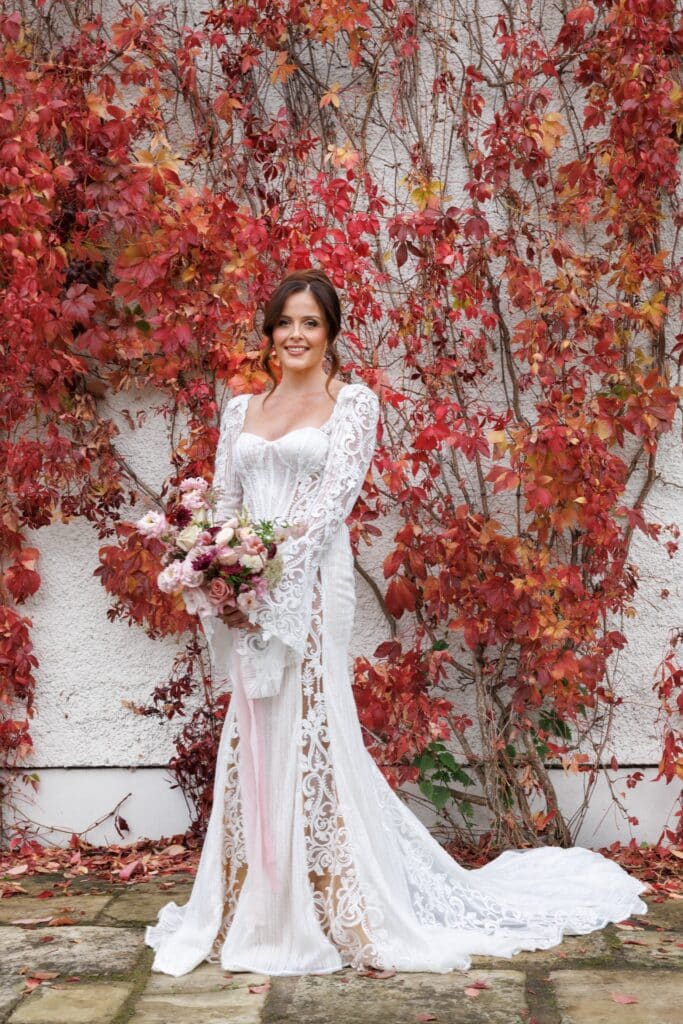 Bride stands in front of red climbing plant at Holesfoot, autumn wedding